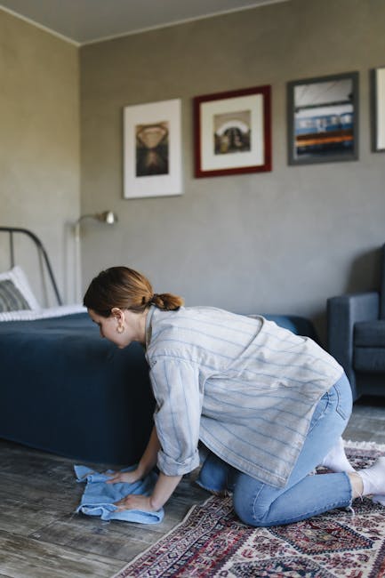 A close-up view of a vacuum cleaner with a black and gray head and a long black hose, being used to clean a decorative patterned carpet in a residential setting. The carpet features floral motifs in m